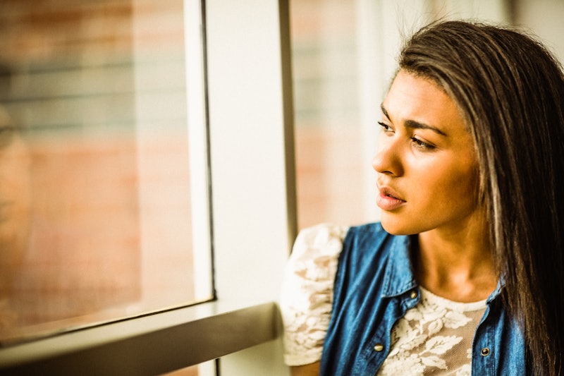 Pretty brunette sitting alone unsmiling against a window