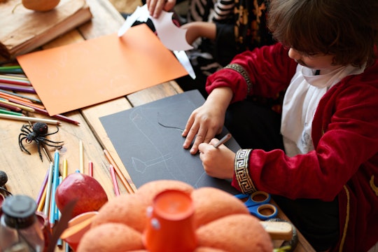 Children in costumes making Halloween decorations out of colored paper in kindergarden