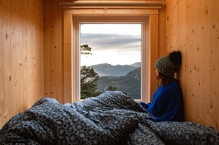 Adventure young girl in a wooden cabin glamping contemplating the landscape through the window