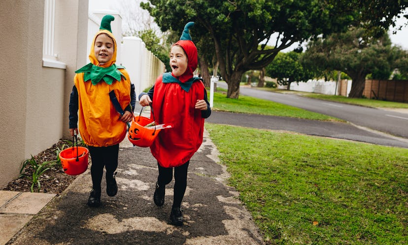 Identical twin sisters in halloween costume with halloween bucket walking on sidewalk. Halloween kid...