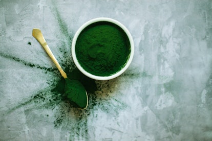 scattered spirulina powder in bowl and spoon on concrete background