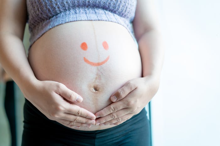 Pregnant woman hold her big stomach with a lovely kids face painting. Concept of wellness of pregna...