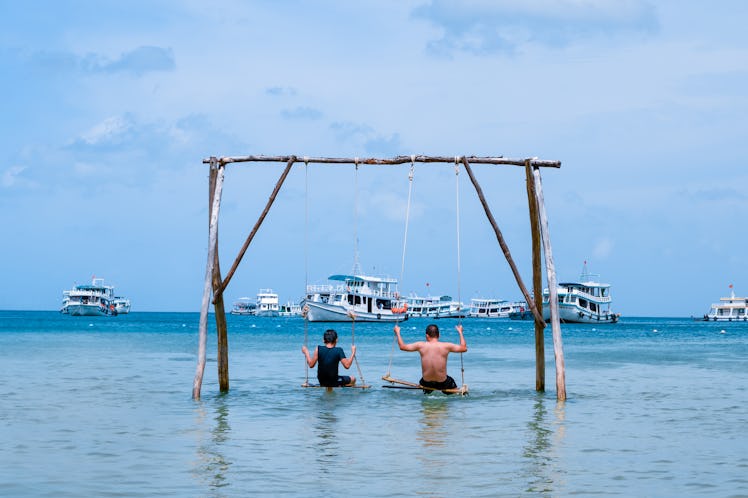 Family, father and son are spending their holidays, swinging on the swing in the sea next to the Bai...