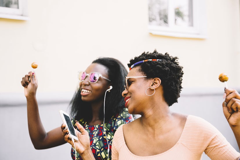 cool girlfriends with lollipop listening to music on headphones in city 