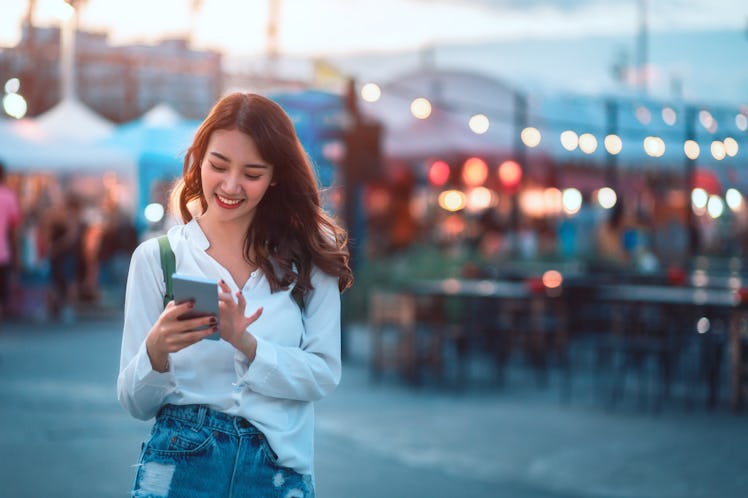 A happy woman at a marketplace, looks at her phone. 