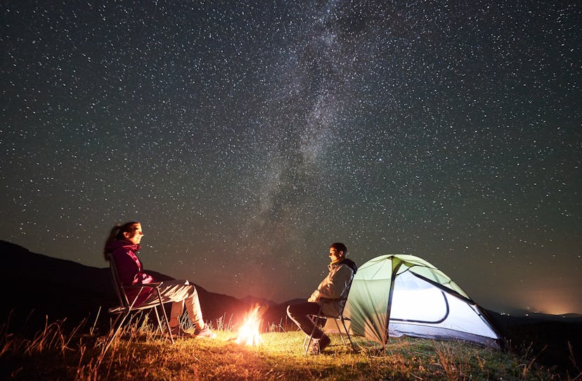 Happy couple tourists resting at summer night camping in the mountains. Smiling man and woman sittin...