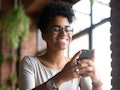 A happy Black woman smiles while texting.