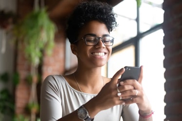 A happy Black woman smiles while texting.