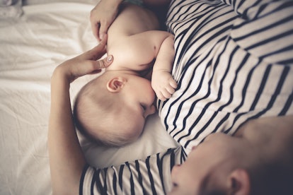 Mom in a striped dress breastfeeds a baby on a white sheet, top view. Concept maternity and breastfe...