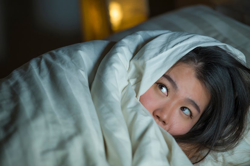 young sleepless beautiful and scared Asian Chinese woman lying on bed awake at night suffering night...