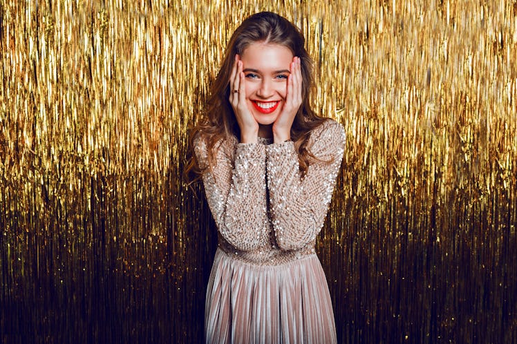 Elegant celebrating woman with surprise  face standing  over  golden sparkling  background. Red lips...