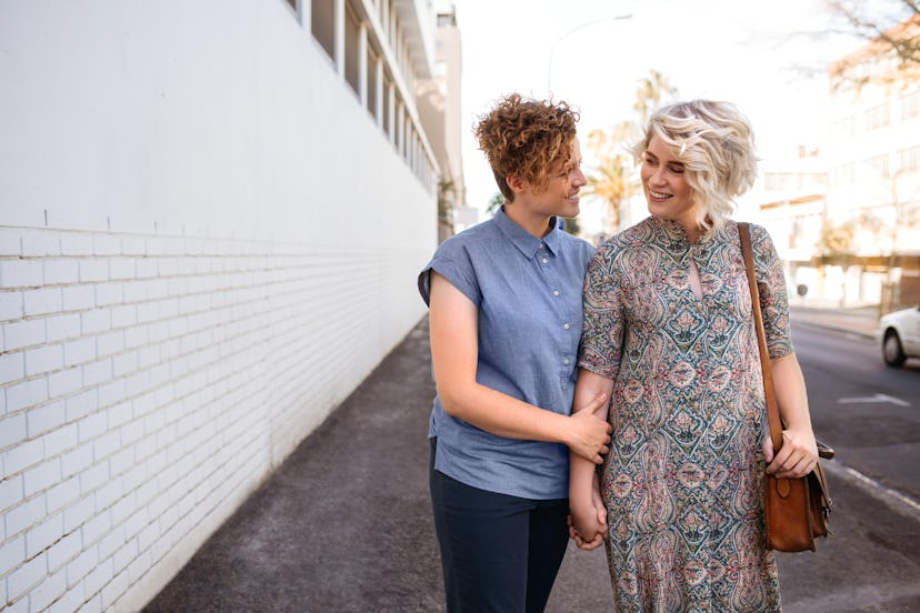 Smiling young lesbian couple walking hand in hand down a street in the city while enjoying a day out...