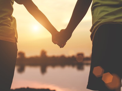 Closeup silhouette of loving couple holding hands while walking at sunset 