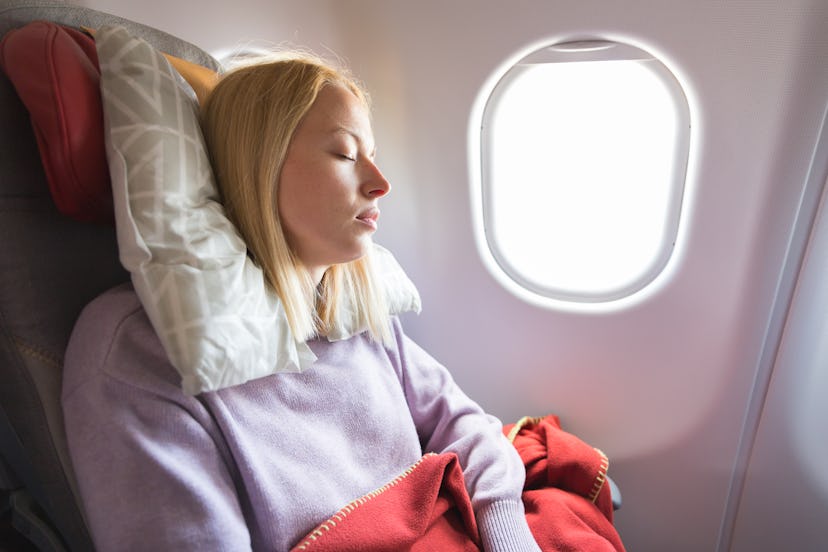 Tired blonde casual caucasian woman sleeping on seat while traveling by airplane on long distance tr...