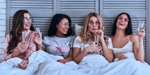 Having fun. Four attractive young women in pajamas drinking cocktails and smiling while lying in the...