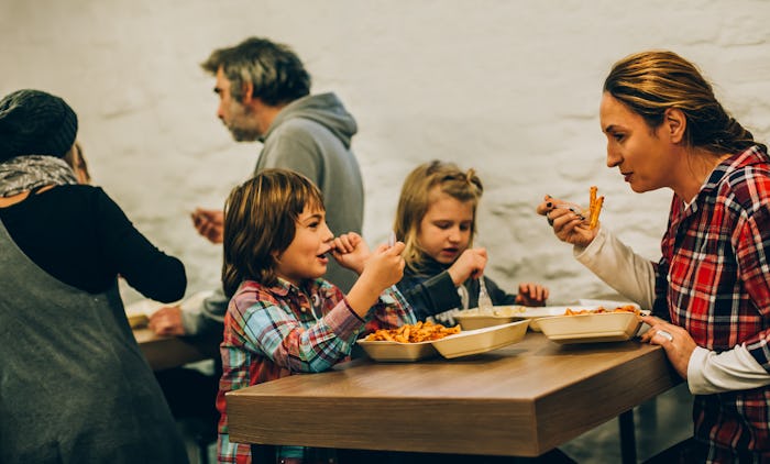 Mother with her children eats spaghetti pasta in fast food restaurant