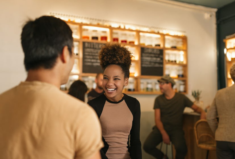 Young African american woman laughing while having a good time in a trendy bar talking with a male f...