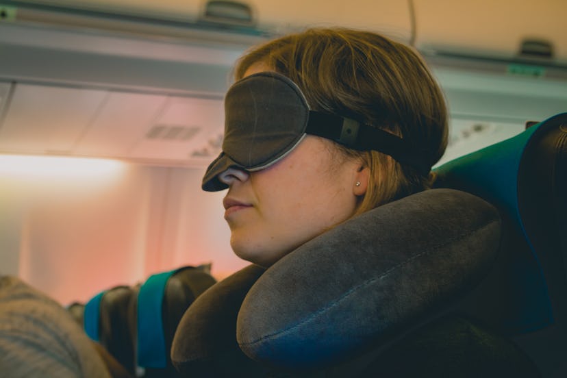 Tired caucasian blond woman with neck pillow and blindfold sleeping on a seat while traveling in a c...