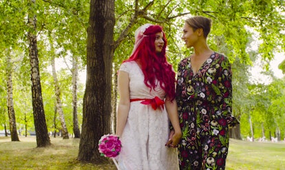 Lesbian wedding. The bride with red hair in a wedding dress and groom are walking in the park hand b...