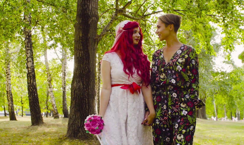 Lesbian wedding. The bride with red hair in a wedding dress and groom are walking in the park hand b...