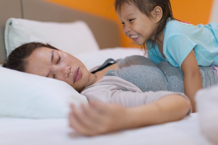A tired mom trying to rest while kid is disturbing her trying to wake her up.