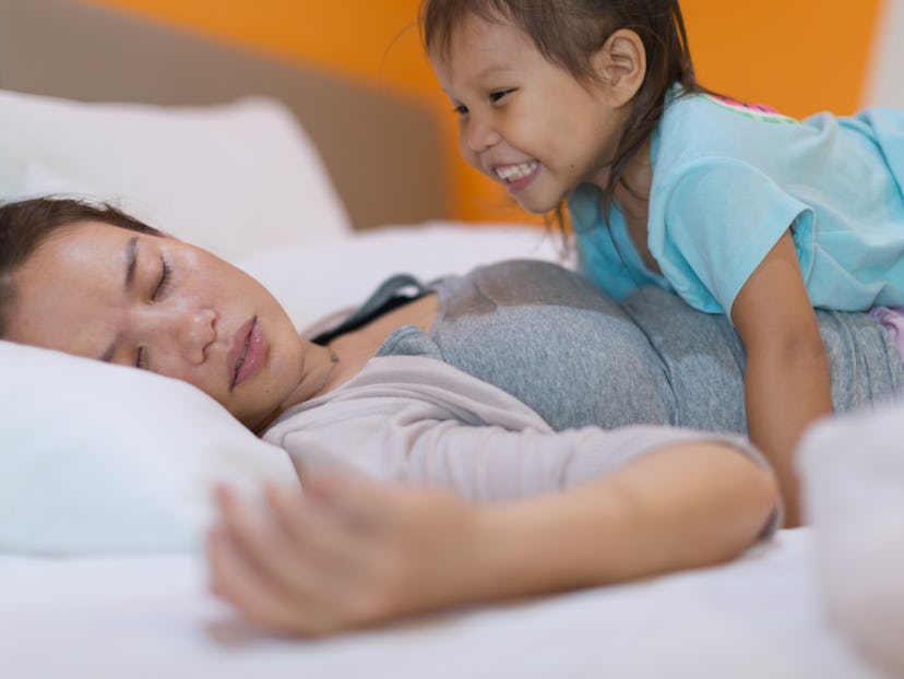 A tired mom trying to rest while kid is disturbing her trying to wake her up.