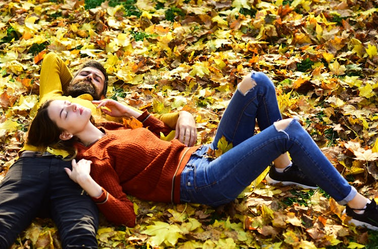Couple in love lies on dry fallen leaves in park. Man and woman with calm faces on grass and leaves ...