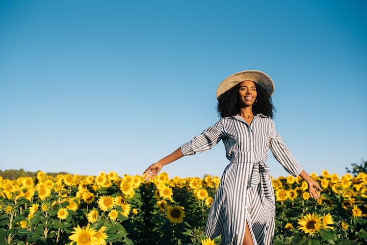 Happy young black woman walking in a sunflower field