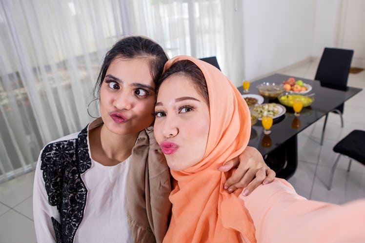 Picture of two Muslim women taking selfie photos with duck face before breaking the fast in the kitc...