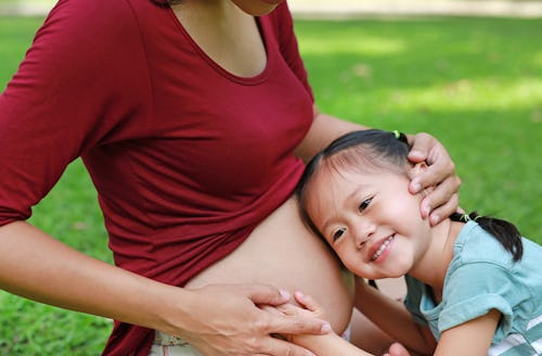 Happy kid girl is hugging pregnant mother's belly in the green garden.