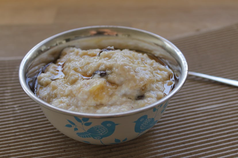 Closeup of banana, raisin and maple syrup oatmeal porridge served in a small white metal bowl decora...