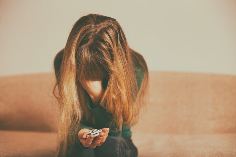 Depressed woman  holding pills while sitting alone at sofa .Toned image.