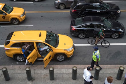 Ride-hailing cars and a a cyclist make their way across 42nd Street as passengers load into a yellow...