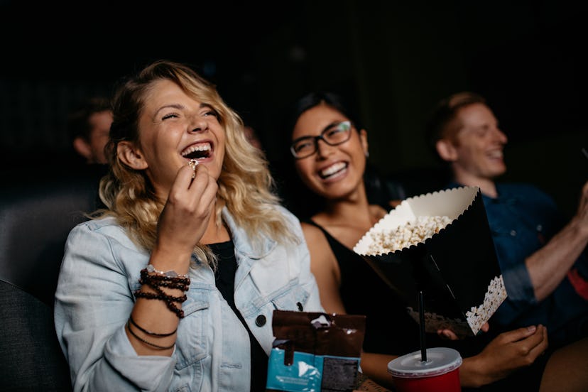 Young woman with friends watching movie in cinema and laughing. Group of people in theater with popc...