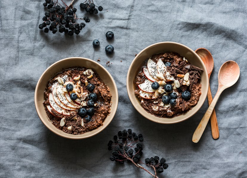 Chocolate oatmeal with apples and blueberries - healthy vegetarian breakfast on a grey background, t...