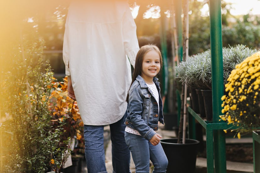 Partial view of woman walking with daughter in sunny day. Outdoor shot of cheerful kid posing in gar...