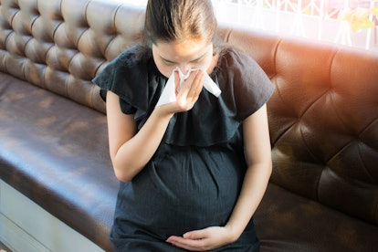 Pretty young pregnant woman feeling sick with a cold and holding a tissue in front of her nose