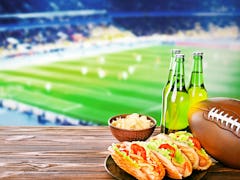 Beer with snack and ball on wooden table against football field background. Sport and entertainment ...