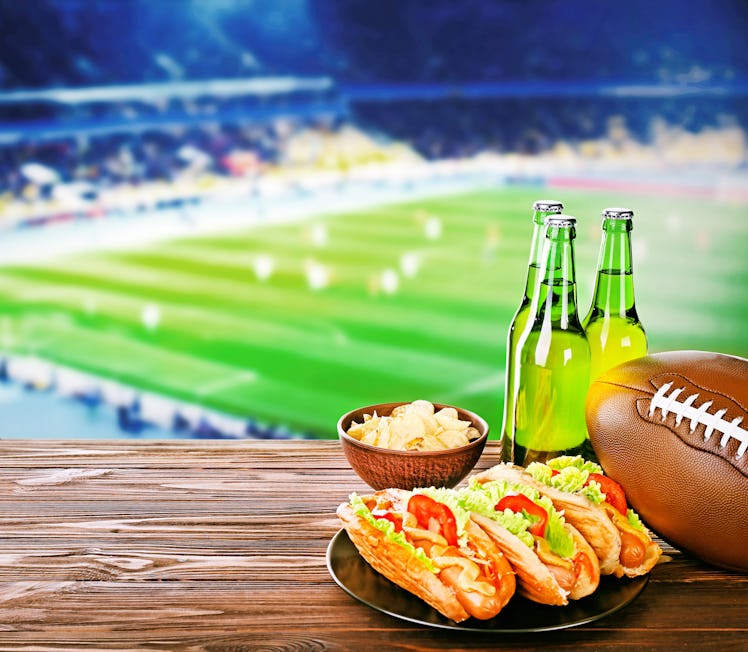 Beer with snack and ball on wooden table against football field background. Sport and entertainment ...