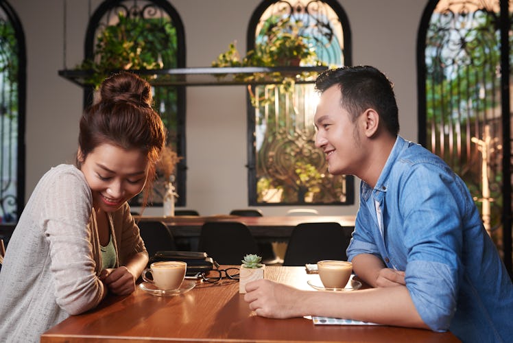 Side view portrait of loving Asian couple meeting in cafe for date, chatting and flirting affectiona...
