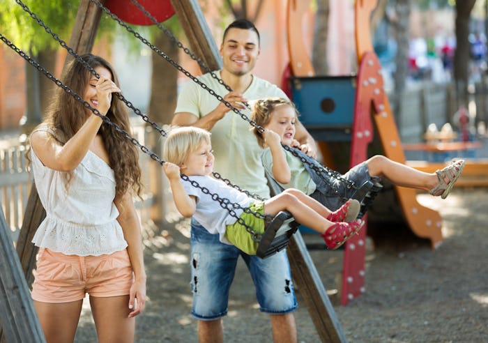 Small daughters on swings with young parents. Focus on woman