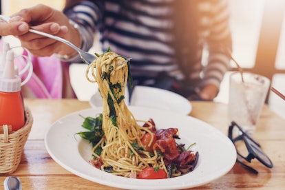 Woman hand showing spaghetti in the dish on the wooden table at restaurant