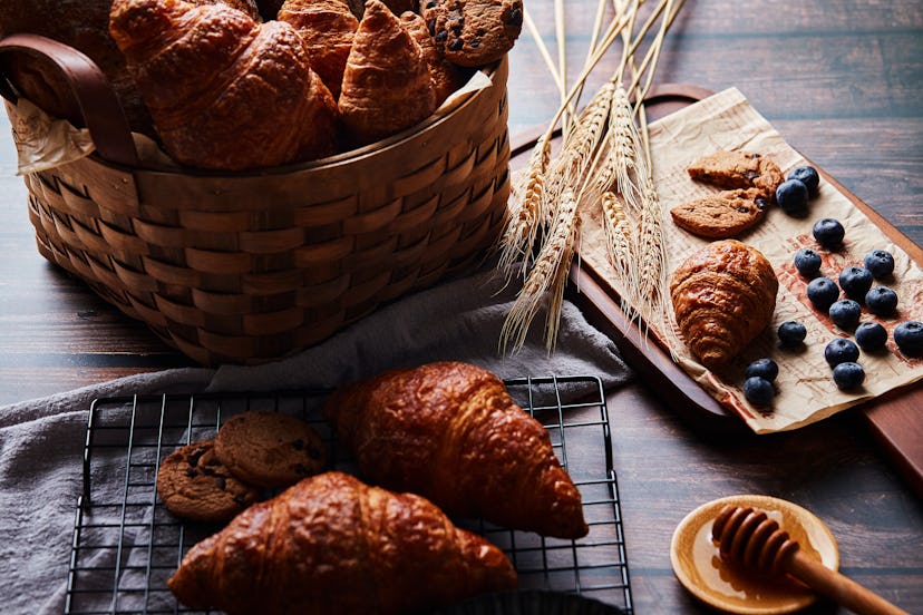 Basket with bread and croissants on the table, croissants and chocolate chip cookies, honey and a bo...
