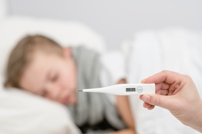 Sick kid with high fever lying in bed and mother taking temperature