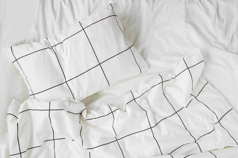 White bedding sheets with striped blanket and pillow. Messy bed. Cozy background.
