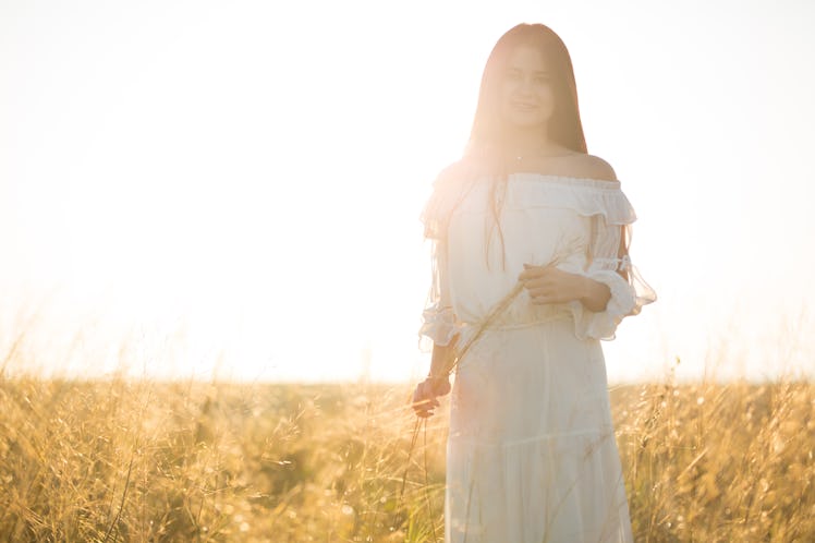 Soft and dreamy image of a young woman with blowing dress in grassy field at sunset