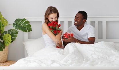 Valentine's Day. happy couple in love with red hert and flowers in bed
