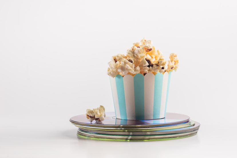 Small bucket of popcorn placed on a stack of movie DVDs. A concept for home theater entertainment.