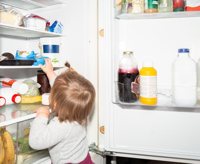 Little baby girl against a refrigerator. Cute one year old baby girl