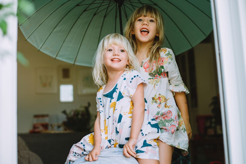 Two little cute sisters laughing together and holding a big green umbrella in a round up of Instagra...